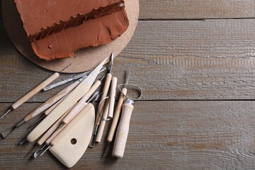 Clay and set of modeling tools on wooden table, flat lay. Space for text