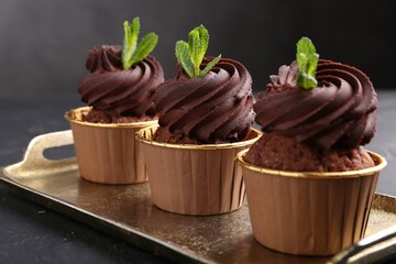 Delicious chocolate cupcakes with mint on black textured table, closeup