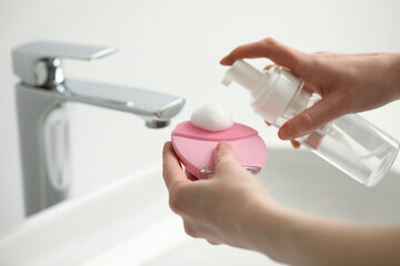 Washing face. Woman applying cleansing foam onto brush above sink in bathroom, closeup