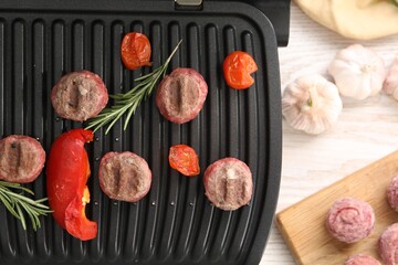 Electric grill with vegetables, meat balls and rosemary on wooden table, flat lay