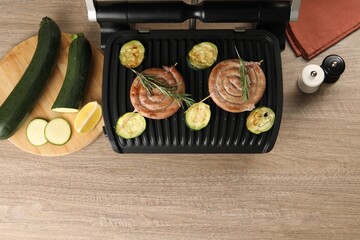 Electric grill with homemade sausages, zucchini and rosemary on wooden table, flat lay. Space for text