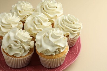 Tasty vanilla cupcakes with cream on beige table, closeup