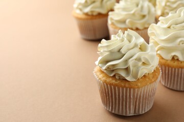 Tasty vanilla cupcakes with cream on beige table, closeup. Space for text