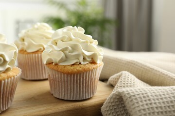 Tasty cupcakes with vanilla cream on wooden board, closeup