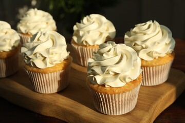 Tasty cupcakes with vanilla cream on wooden table, closeup
