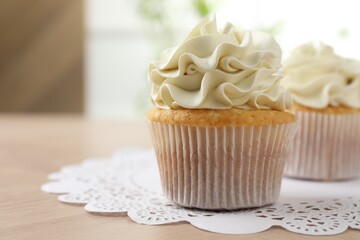 Tasty cupcakes with vanilla cream on light wooden table, closeup