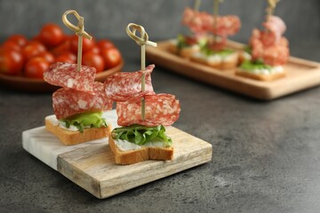 Tasty canapes with salami, greens and cream cheese on grey table. Space for text