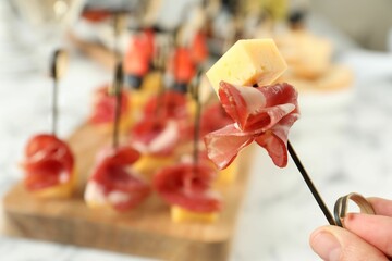 Naklejka na ściany i meble Woman holding tasty canape with cheese and prosciutto on table, closeup. Space for text