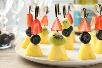 Tasty canapes with pineapple, kiwi and berries on light wooden table, closeup