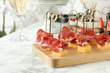Tasty canapes with cheese and ham on white marble table, closeup. Space for text