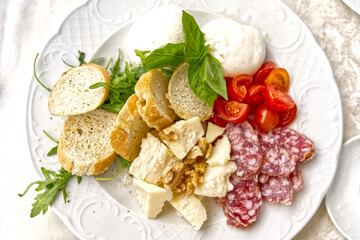 Traditional Italian food served on a plate, salami cheese, herbs, baguette, tomatoes