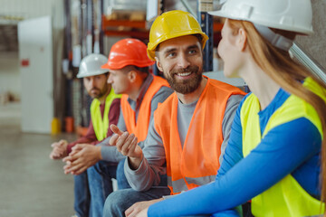 Happy bearded man and attractive woman wearing hard hat and work wear talking during break, relaxing