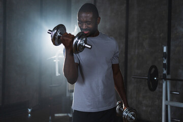 Fitness workout in gym. African American man bodybuilder picking up dumbbells in gym. Workout...