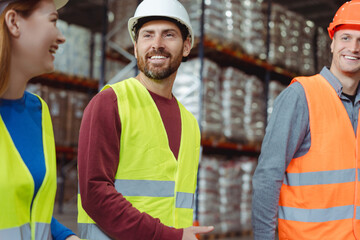Attractive, bearded man wearing hard hat, vest talking to colleagues, discussing productivity