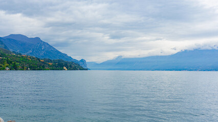 The largest Italian lake Garda in northern Italy. Small towns around a lake surrounded by cloud-covered Alps. Landscapes of Italy. The Alps towering over Europe. Overcast weather. Snowy peaks