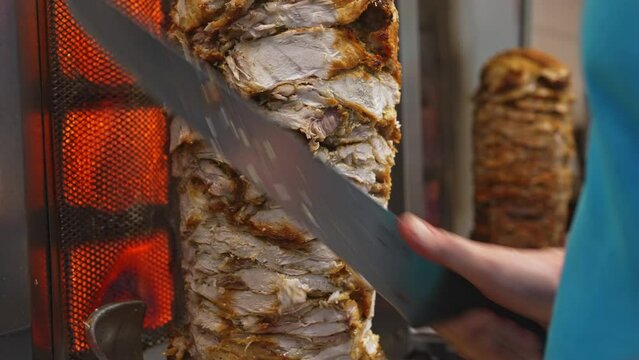 Man cutting juicy meat on shawarma spit.