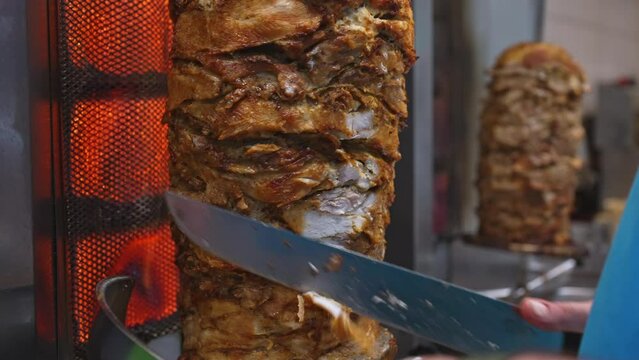 Man cutting juicy meat on shawarma spit.