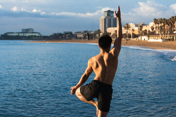 young man making yoga exercises on beach from back