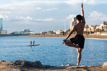 Attractive young man practicing yoga meditation at beach