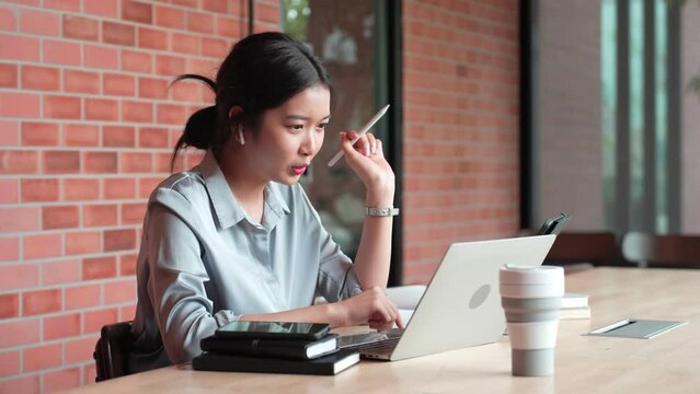 The young Asian businesswoman is having a work discussion via video call, using her laptop to conference with her colleagues at her office