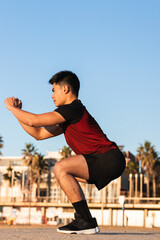 Asian guy is doing squats outside. Sports training at park, workout outdoors