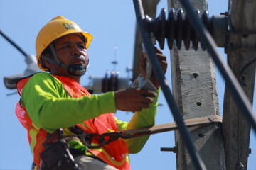 A man in a yellow helmet is working on a power line