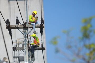 A man in a yellow helmet is working on a power line