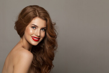 Naklejka premium Elegance fashionable redhead woman with long wavy hair and make-up. Studio headshot portrait of fashion model lady with red colorful shine lipstick. Haircare, skin care and coloration concept