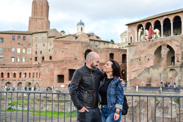 Fototapeta na wymiar Happy Beautiful Tourists couple traveling at Rome, Italy, near Ancient Trajan's Market, ruins in Via dei Fori Imperial Visiting Italy - man and woman enjoying weekend weekend vacation 