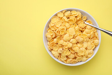 Breakfast cereal. Tasty corn flakes in bowl and spoon on yellow table, top view. Space for text