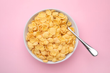 Breakfast cereal. Tasty corn flakes in bowl and spoon on pink table, top view