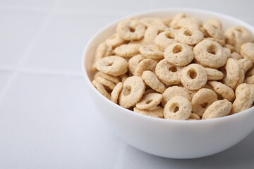 Tasty cereal rings in bowl on white table, closeup. Space for text