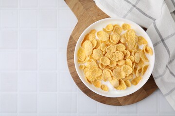 Breakfast cereal. Tasty corn flakes with milk in bowl on white tiled table, top view. Space for text