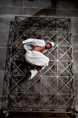 Energetic African American male dancer jumps and twirls in a studio wearing white attire, executing...