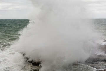 Immense waves hitting a large rock at the edge of the beach. Force of nature.