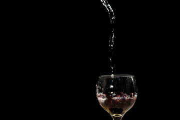 Water in streams and drops falling into a wine glass with grapes inside.