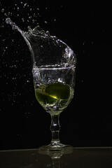 Splashes coming out of a glass cup with clear water caused by a slice of lemon. Isolated on dark background.