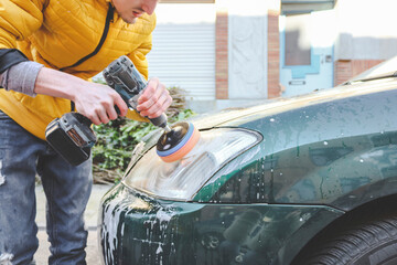 A young caucasian guy in a yellow jacket is drilling a drill with a disk with a sponge and...