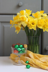 Bouquet of golden daffodils in a glass vase on green wooden background with space for text. 