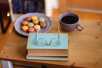 Purple plate filled with pastel macarons, cup of tea or coffee, vintage books and reading glasses...