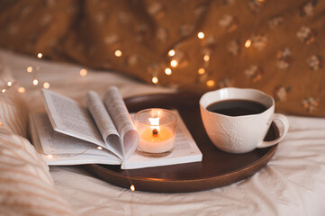 Cup of coffee with open paper book with folded pages in heart shape and burning scented candle over...