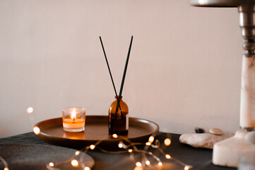 Home liquid perfume in glass bottle with sticks and burning scented candle on wooden tray on table...