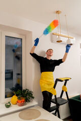 in the apartment cleaner in a yellow apron is cleaning a chandelier with a dust brush