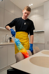 in the apartment cleaner in a yellow apron is cleaning chairs with a dust brush
