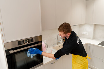 Obraz premium in an apartment cleaner in a yellow apron is cleaning the oven with a blue rag
