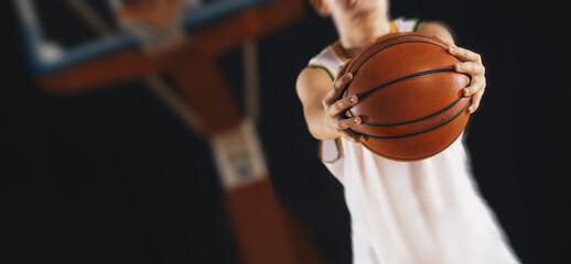 Young basketball player with classic ball. Basket in background. Junior level basketball player holding game ball. Basketball training session for kids