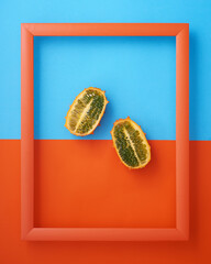 Horned melon in picture frame on blue and orange background