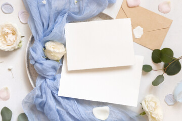 Cards near light blue tulle fabric knot and cream roses on plates top view copy space, wedding...