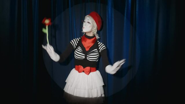 Female mime artist standing in spotlight on stage and pretending like conducting orchestra with flower instead of baton during comedy performance in theatre