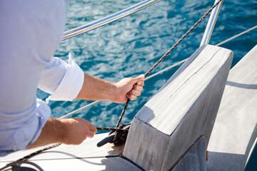 Man sailing on yacht on sea in summer vacation. Close up of hands with rope. Traveler enjoying adventure, freedom. Sailor spread sails. Lifestyle moment on ecological transport in sustainable travel